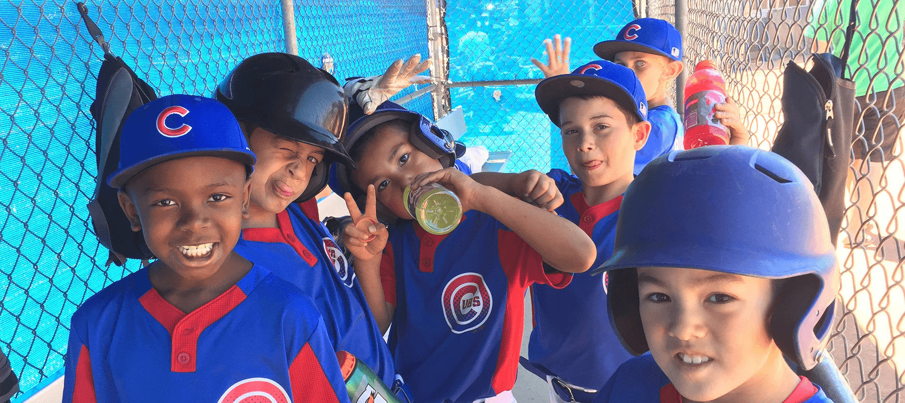 Young baseball players in blue Cubs uniforms making silly faces and smiling in a dugout.